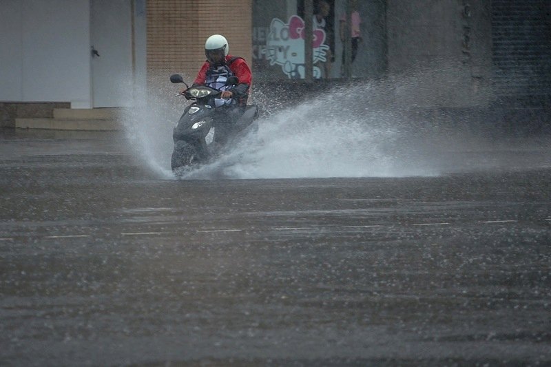 颱風利奇馬暴風圈9日影響台灣北部及東北部陸地，台北市上午出現間歇性降雨，民眾騎車出門，路上濺起大量水花。(圖：中央社)