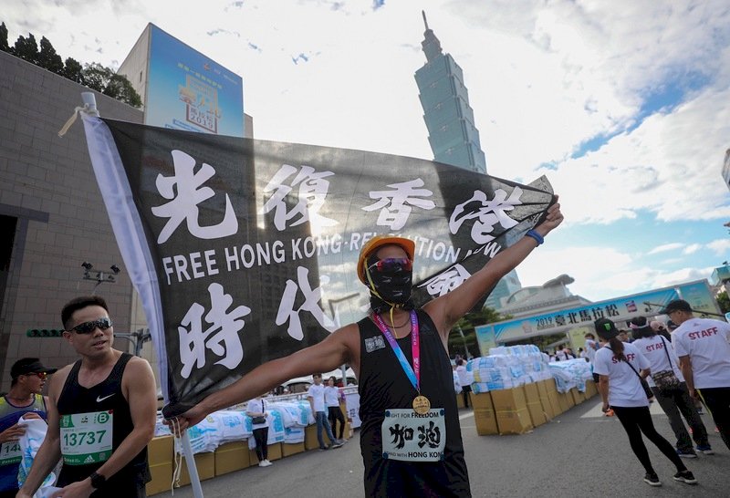 2019台北馬拉松15日在台北市政府前廣場開跑，吸引2萬8000名國內外跑者共襄盛舉，1名跑者完賽後揮舞標語旗幟為香港加油。