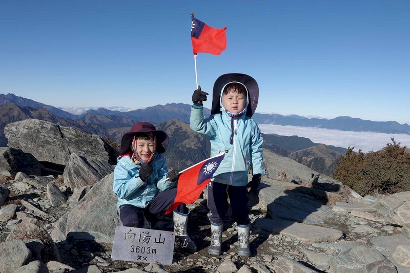 住在新北市的7歲阿興、5歲阿賢兄弟,今年1月初與父母一起攀登百岳排名16、海拔3603公尺的向陽山,登頂時兩人揮舞國旗,模樣萌翻天。(邱德鑫提供)