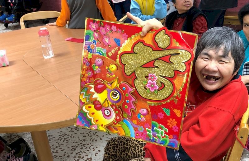 過年家家團圓,花蓮黎明教養院為院生安排春節布置活動,院生開心拿著春聯拍照。(黎明教養院提供)