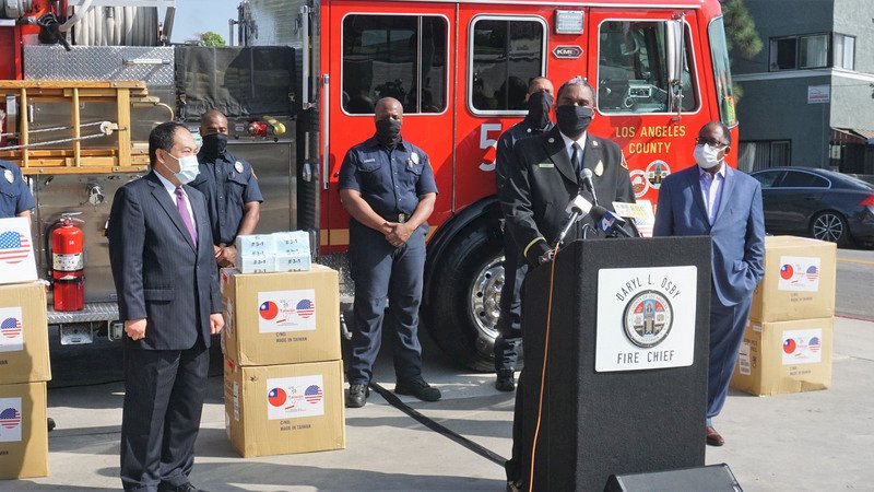 駐洛杉磯台北經濟文化辦事處處長黃敏境（前左）23日代表台灣政府捐3萬5000片口罩給洛杉磯郡消防局，他致詞時說「我們都是洛杉磯人」。前右為洛杉磯郡長瑞德里．湯瑪斯（Mark Ridley-Thomas）、講台上為郡消防局長歐斯比（Daryl Osby）。