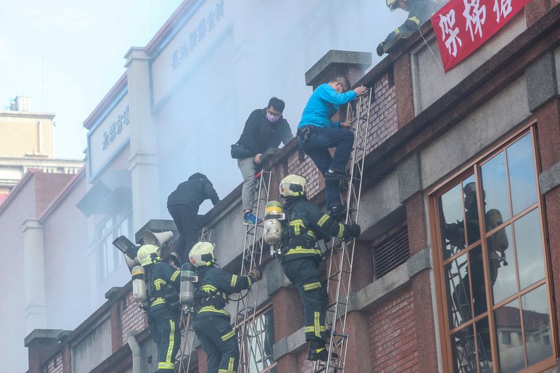 台北市消防局「一年一度年貨大街消防演習」22日在永樂市場舉辦,情境演習假設永樂市場商家桶裝瓦斯破裂爆炸起火引燃攤架,火勢延燒到永樂市場,消防人員架梯實施人員救助。 (圖:中央社)