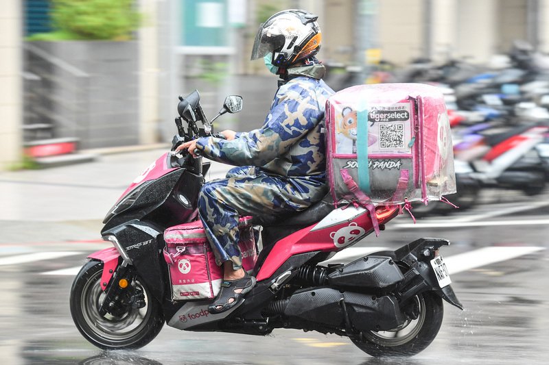 國內疫情升溫，為防群聚，民眾使用美食外送平台需求增加。台北市18日午後下起大雨，外送員全副武裝，在風雨中接單送貨。 (圖：中央社)